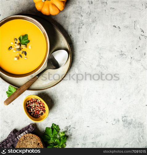 Vegetarian autumn pumpkin cream soup with seeds on grey concrete background, flat lay, space for text. Pumpkin cream soup with seeds, flat lay composition