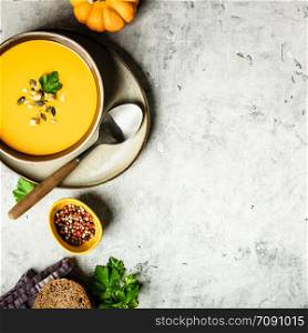 Vegetarian autumn pumpkin cream soup with seeds on grey concrete background, flat lay, space for text. Pumpkin cream soup with seeds, flat lay composition