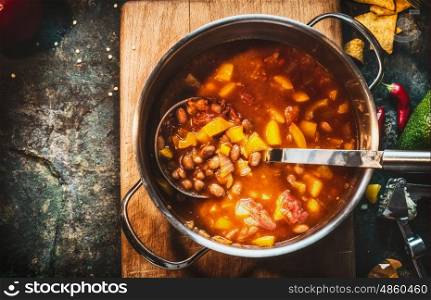 Vegetarian Bean soup in cooking pot with ladle on dark rustic background, top view, close up, place for text. Mexican cuisine