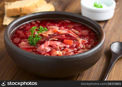 Vegetarian Borscht soup of Ukrainian origin made of beetroot, carrot, cabbage, potato, onion and celery in rustic bowl, photographed on dark wood with natural light (Selective Focus, Focus in the middle of the soup)