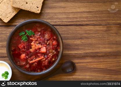 Vegetarian Borscht soup of Ukrainian origin made of beetroot, carrot, cabbage, potato, onion and celery in rustic bowl, with wholegrain bread and sour cream on the side, photographed overhead with natural light (Selective Focus, Focus on the soup)