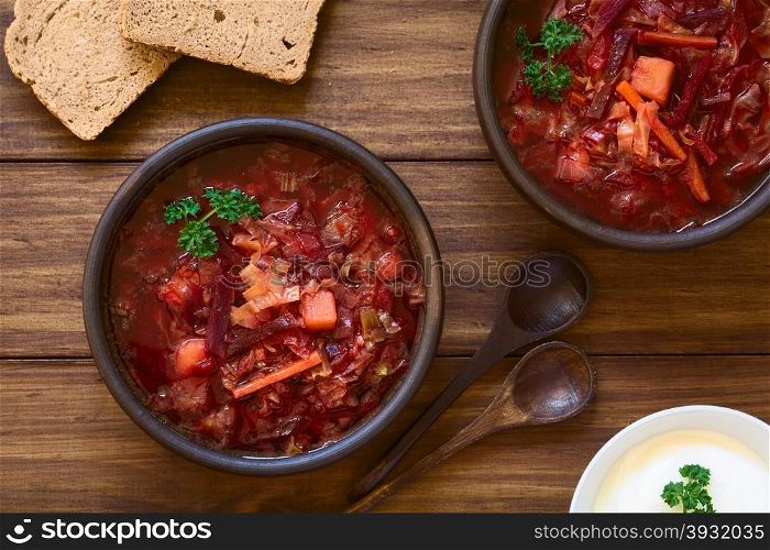 Vegetarian Borscht soup of Ukrainian origin made of beetroot, carrot, cabbage, potato, onion and celery in rustic bowls, with wholegrain bread and sour cream on the side, photographed overhead with natural light (Selective Focus, Focus on the soup)