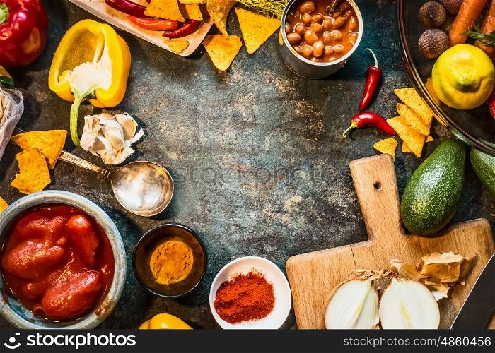 Vegetarian cooking ingredients for Mexican cuisine: canned Beans, Peeled tomatoes, paprika,chili, onion,lemon, spices , avocado and tacos or tortilla chips on dark rustic background, top view, frame