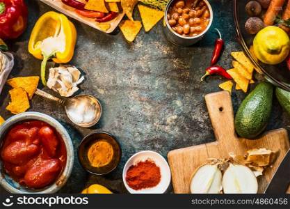 Vegetarian cooking ingredients for Mexican cuisine: canned Beans, Peeled tomatoes, paprika,chili, onion,lemon, spices , avocado and tacos or tortilla chips on dark rustic background, top view, frame