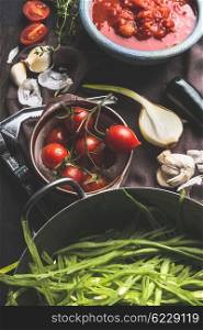 Vegetarian cooking ingredients in bowls. Green french beans, tomatoes, garlic,onion on dark rustic kitchen wooden table. Vegan and healthy food concept. Country food