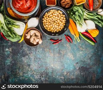 Vegetarian cooking ingredients with chick peas dish, spicy indian curry paste , greens, ginger and vegetables on rustic background, top view, border. Healthy food and eating or Indian cuisine concept