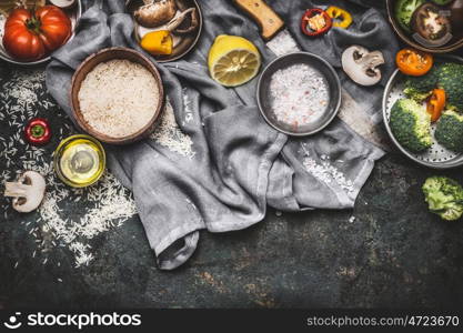 Vegetarian cooking ingredients with lemon, rice and vegetables on dark rustic background, top view, border. Healthy or diet food concept