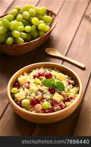 Vegetarian couscous salad with grapes, pomegranate, walnuts, cheese, lime and mint in wooden bowl photographed with natural light (Selective Focus, Focus on the mint leaf on the dish)