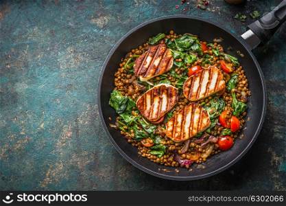 Vegetarian food concept. Healthy lentil dish with spinach and fried cheese in cooking pan on rustic background with ingredients, top view.