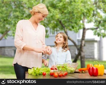 vegetarian food, culinary, family and people concept - happy mother and daughter cooking vegetable salad for dinner over summer house background