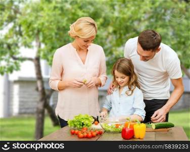 vegetarian food, culinary, happiness and people concept - happy family cooking vegetable salad for dinner over house and summer garden background
