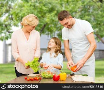 vegetarian food, culinary, happiness and people concept - happy family cooking vegetable salad for dinner over over summer house background