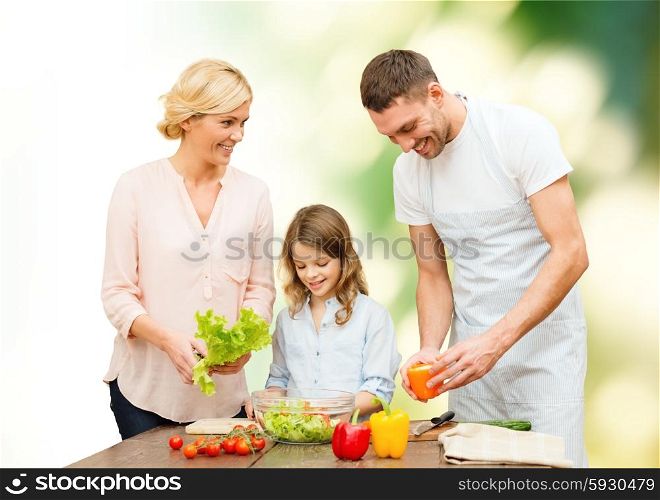 vegetarian food, culinary, happiness and people concept - happy family cooking vegetable salad for dinner green natural background