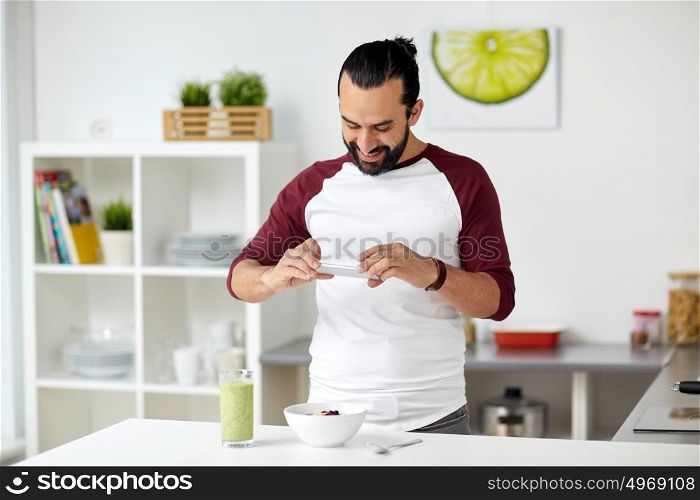 vegetarian food, healthy eating, people, technology and breakfast concept - man with smartphone photographing muesli with vegetable smoothie at home kitchen. man photographing breakfast by smartphone at home