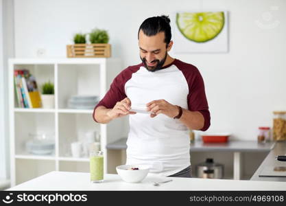 vegetarian food, healthy eating, people, technology and breakfast concept - man with smartphone photographing muesli with vegetable smoothie at home kitchen. man photographing breakfast by smartphone at home