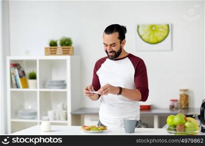 vegetarian food, healthy eating, people, technology and breakfast concept - man with smartphone photographing vegetable sandwiches at home kitchen. man photographing food by smartphone at home