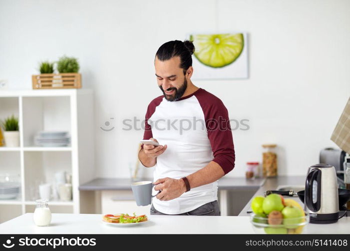 vegetarian food, healthy eating, people, technology and breakfast concept - man with smartphone, coffee and vegetable sandwiches at home kitchen. man with smartphone having breakfast at home