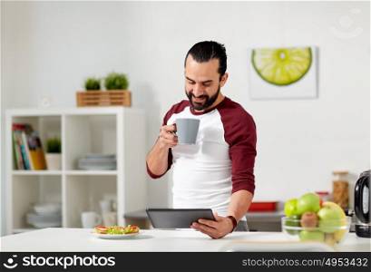 vegetarian food, healthy eating, people, technology and diet concept - man having vegetable sandwiches with coffee for breakfast and looking to tablet pc computer at home kitchen. man with tablet pc eating at home kitchen