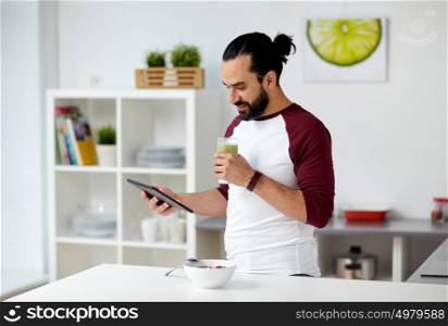vegetarian food, healthy eating, people, technology and diet concept - man having muesli with vegetable smoothie for breakfast and looking to tablet pc computer at home kitchen. man with tablet pc eating breakfast at home