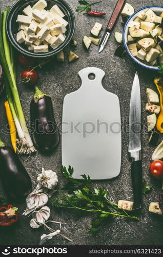 Vegetarian food ingredients with vegetables, herbs, feta cheese, spices and kitchen knife around cutting board, top view, frame. Layout for healthy clean eating and cooking or diet nutrition concept