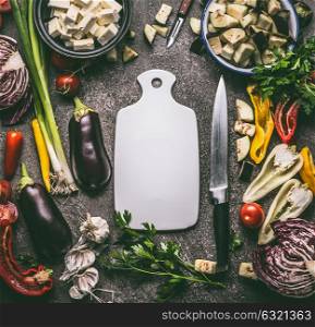 Vegetarian food ingredients with vegetables, herbs, spices and kitchen knife around cutting board, top view, frame. Layout for healthy clean eating and cooking or diet nutrition concept