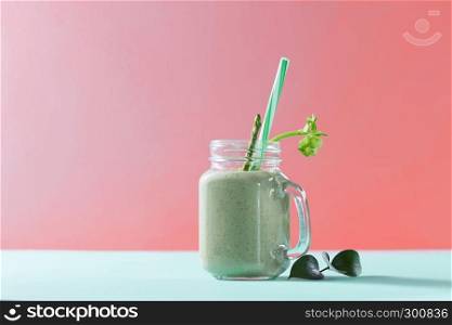 Vegetarian healthy mix from vegetables with green leaves and plastic straw in a glass jar on duotone background in a color of the year 2019 Living Coral Pantone.. Green homemade smoothie from organic vegetables with asparagus and celery in a mason jar on duotone background in color of the year 2019 Living Coral Pantone