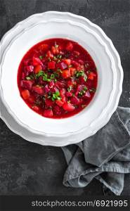 Vegetarian hot diet beetroot soup with vegetables on plate, top view, dark background