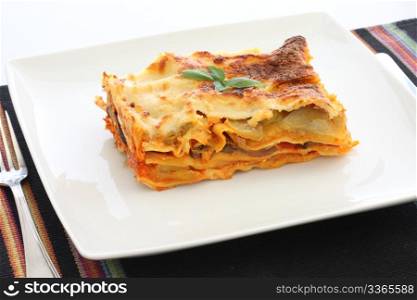 Vegetarian lasagna with eggplant, courgette, sweet potatoes and tomato sauce on a white plate.