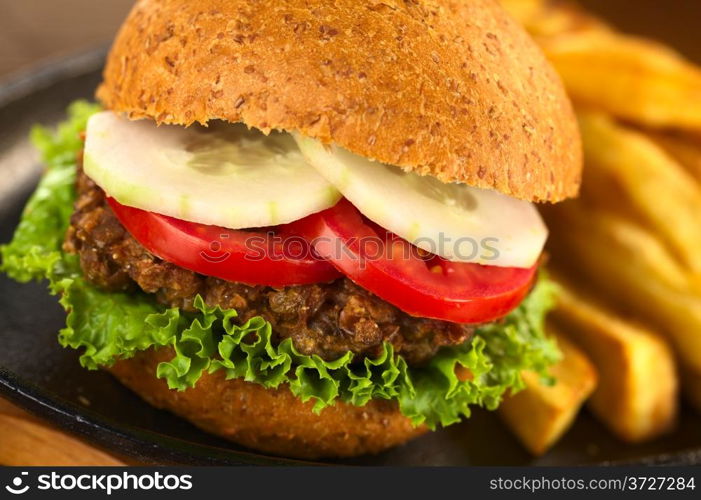 Vegetarian lentil burger in wholewheat bun with lettuce, tomato and cucumber accompanied by French fries (Selective Focus, Focus on the front of the lettuce, lentil burger, tomato and cucumber) . Vegetarian Lentil Burger