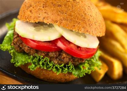 Vegetarian lentil burger in wholewheat bun with lettuce, tomato and cucumber accompanied by French fries (Selective Focus, Focus on the front of the lettuce, lentil burger, tomato and cucumber) . Vegetarian Lentil Burger