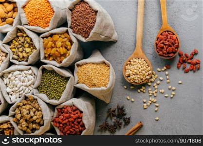 Vegetarian products. Top flat view of small hessian sacks filled with raisins, goji, almond, mulberry and other cereals, star anise near, two wooden spoons