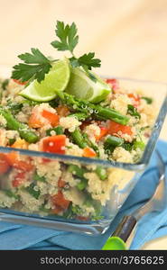 Vegetarian quinoa dish with green asparagus and red bell pepper, garnished with lime wedges and parsley leaf, served in glass bowl (Selective Focus, Focus on the asparagus head on the dish)