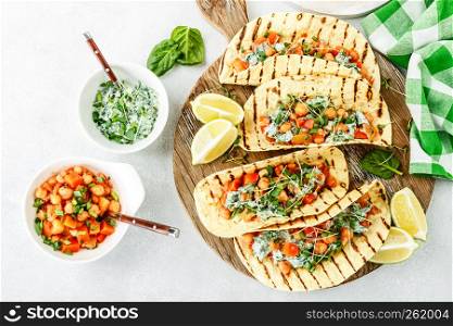 vegetarian snack of tacos with chickpea curry and sour cream sauce with parsley, spinach, green onions and sprouted flax seeds. healthy plant based food. top view on light background, flat lay