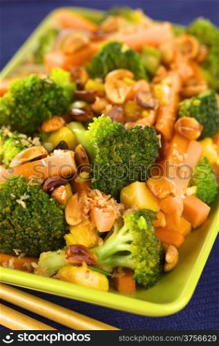 Vegetarian stir-fry Thai-style with broccoli, carrot, onion, mango with fried coconut flakes and peanuts (Selective Focus, Focus on the broccoli in the middle of the image). Vegetable Stir-Fry Thai-Style