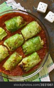 Vegetarian stuffed savoy cabbage rolls filled with wholegrain rice, pepper, onion and carrot, baked on tomato sauce in pan, photographed overhead on slate with natural light (Selective Focus, Focus on the dish)