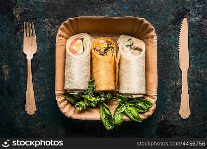 Vegetarian tortilla wraps in paper plate and wooden cutlery on dark background, top view, close up. Healthy lunch snack or street food concept
