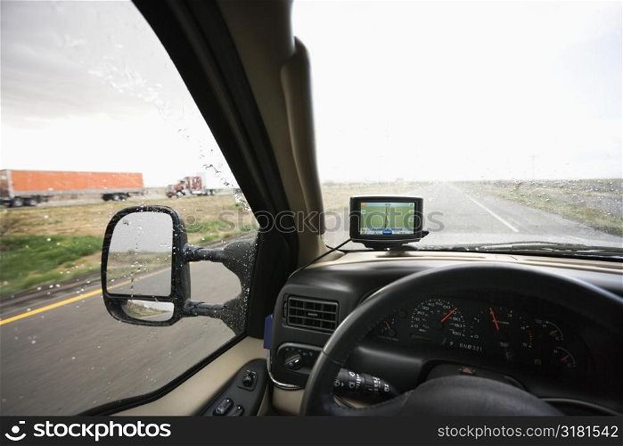 Vehicle dashboard with GPS and view through windshield of rainy highway ahead.