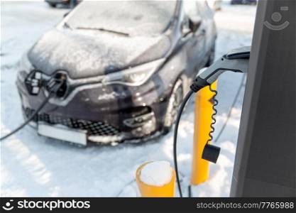vehicle, power and green energy concept - close up of electric car charging battery in winter. close up of electric car charging in winter