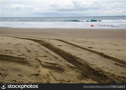 Vehicle tracks at a beach with a red warning flag