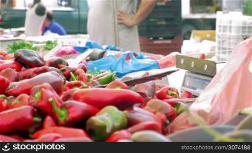 Vendors selling red sweet pepper on street market. Woman paying for vegetables, getting change and taking the packet. Seller adding peppers on the stall