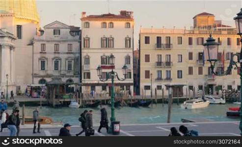 Venetian Grand Canal with water transport, old buildings and people walking along it