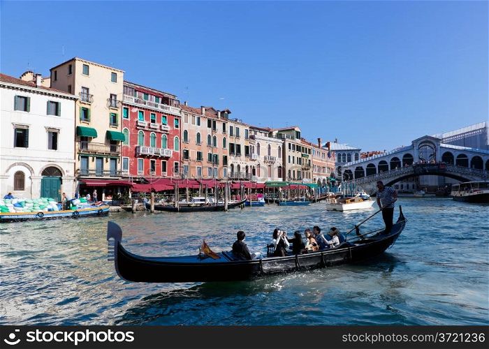 Venice, Italy. Gondola with tourists floats on Grand Canal, Italian Canal Grande at sunny summer day. Rialto bridge in the background