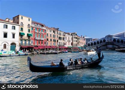 Venice, Italy. Gondola with tourists floats on Grand Canal, Italian Canal Grande at sunny summer day. Rialto bridge in the background