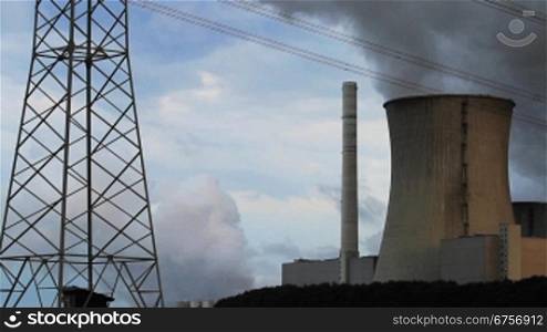Verkohlter Rauch von Tnrmen eines Kohlekraftwerks steigt in die Luft inmitten von einem Strommast und Stromkabel