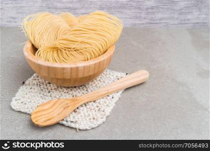 Vermicelli pasta nests in wooden bowl on cement background