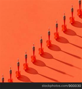 Vertical darts in a diagonal line with shadows on an orange background, copy space.. Diagonal line of darts with shadows.