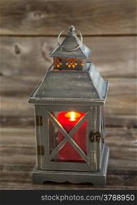 Vertical front view of an old Asian design lantern with red candle burning brightly inside on rustic wood