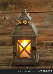 Vertical front view of an old Asian design lantern with white candle glowing brightly inside on rustic wood