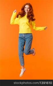 Vertical full-length portrait cheerful redhead excited girl jumping and feeling happy, smiling gazing camera carefree, cant wait open presents on winter holidays party, orange background.. Vertical full-length portrait cheerful redhead excited girl jumping and feeling happy, smiling gazing camera carefree, cant wait open presents on winter holidays party, orange background