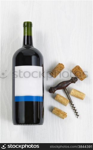 Vertical image a large bottle of red wine with an antique corkscrew with old corks on white wood.